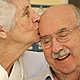 Elder woman kissing smiling husband on forehead.